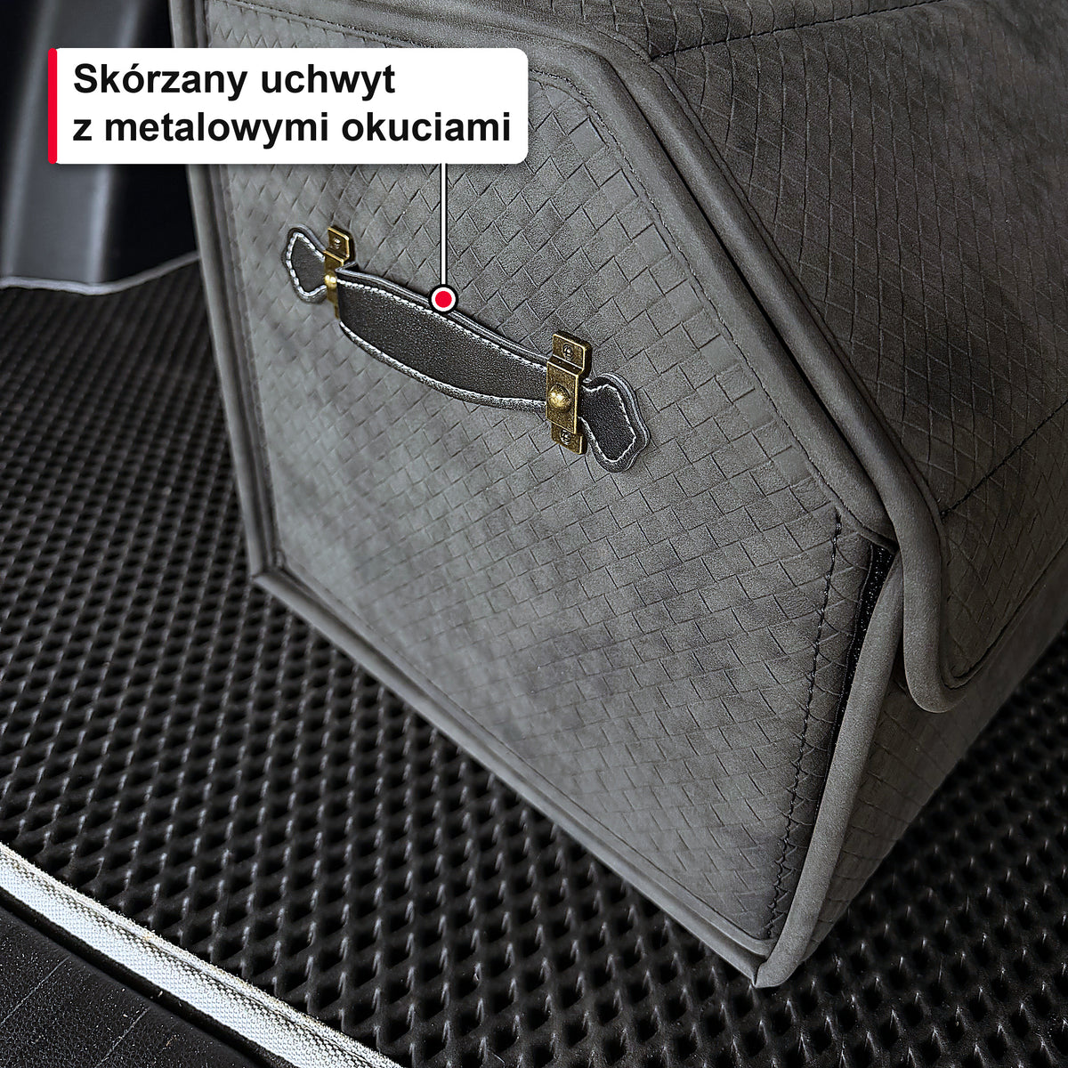 Zbliżenie na skórzany uchwyt z metalowymi okuciami na szarym organizerze do bagażnika